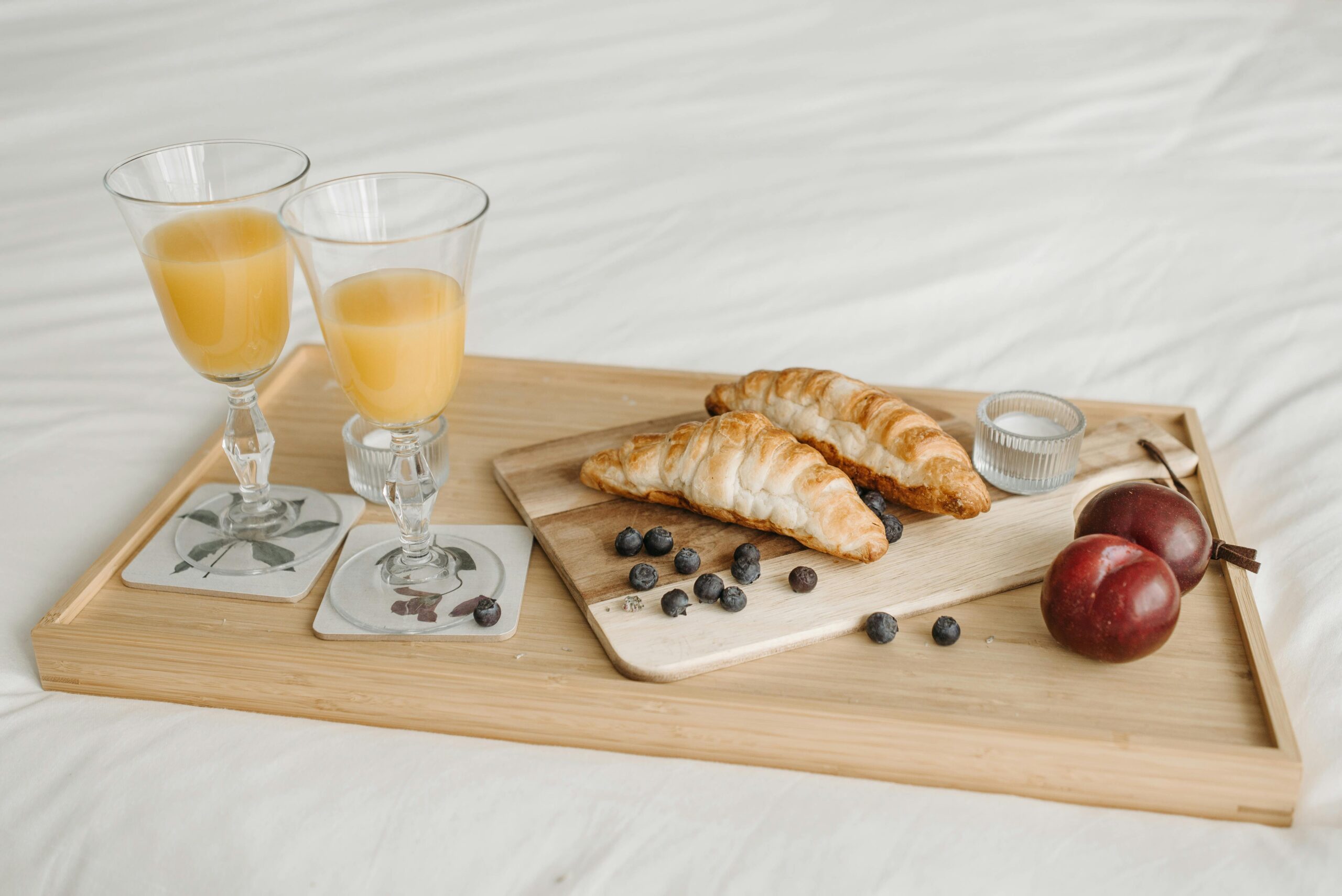 Delightful breakfast setting with croissants, fresh juice, and fruits on a wooden tray.